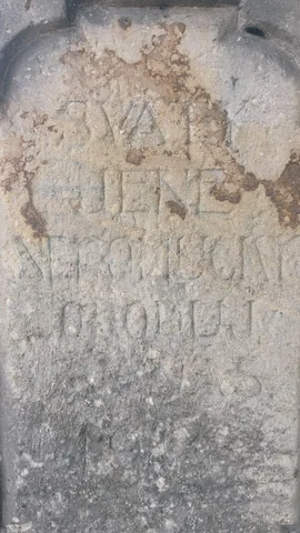 Detail silně zvětralého nápisu na kameni; rozeznatelná jsou jen některá písmena a celý text nelze bezpečně přečíst.